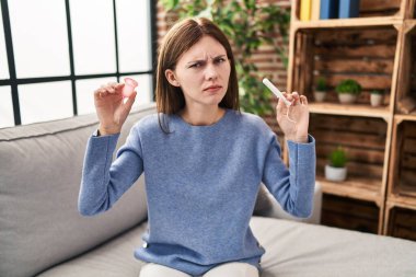 Young brunette woman holding menstrual cup and tampon skeptic and nervous, frowning upset because of problem. negative person. 
