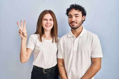 Young couple wearing casual clothes standing together showing and pointing up with fingers number three while smiling confident and happy. 