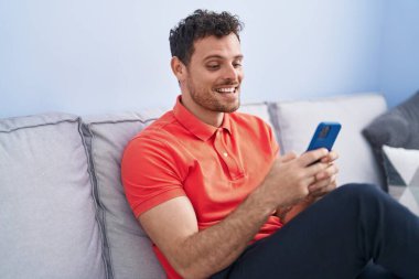 Evdeki kanepede oturan, akıllı telefon kullanan genç bir İspanyol.