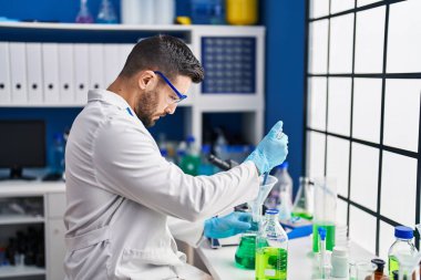 Laboratuvarda sıvı ölçen bilim adamı üniforması giyen İspanyol genç adam.