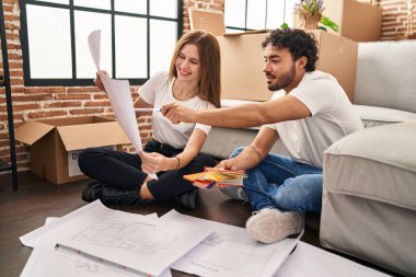 Erkek ve kadın, gülümseyen ve kendine güvenen bir çift yeni evinde boya rengi seçiyor.