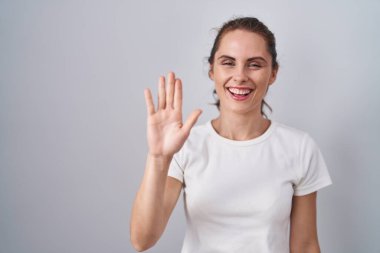 Güzel esmer kadın izole edilmiş arka planda duruyor. Mutlu ve güler yüzlü bir şekilde selam veriyor. 