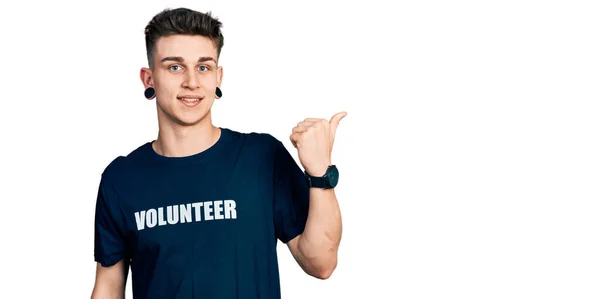 stock image Young caucasian boy with ears dilation wearing volunteer t shirt pointing to the back behind with hand and thumbs up, smiling confident 