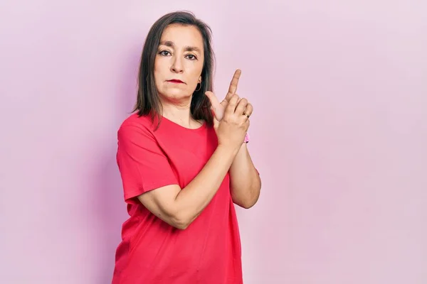 Middle age hispanic woman wearing casual clothes holding symbolic gun with hand gesture, playing killing shooting weapons, angry face