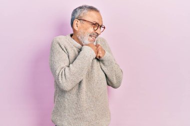 Sakallı, sıradan bir süveter ve gözlüklü yakışıklı, gergin ve heyecanlı elleri çenesinde yan tarafa bakıyor. 