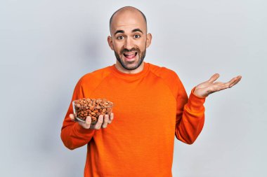 Fıstık tutan genç kel adam başarıyı mutlu bir gülümsemeyle ve kazanan yüz ifadesiyle kutluyor. 