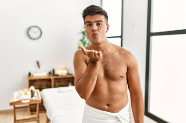İspanyol asıllı genç adam spa merkezinde üstsüz duruyor kameraya bakıyor ve havada bir öpücük savuruyor güzel ve seksi. aşk ifadesi. 