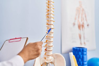 Orta yaşlı İspanyol kadın fizyoterapist rehabilitasyon kliniğinde omurganın anatomik modelini gösteriyor.