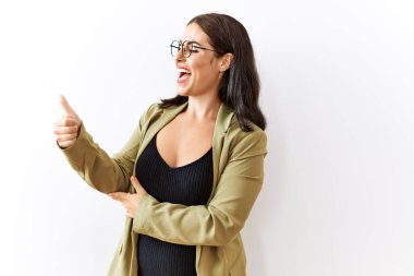 Genç esmer kadın izole edilmiş arka planda duruyor. Gururlu görünüyor, gülümsüyor. Kenarda baş parmak hareketi yapıyor. 