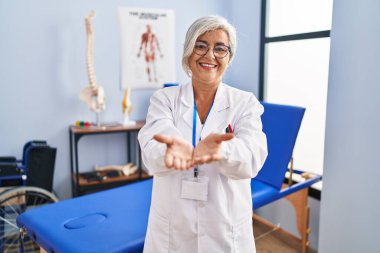 Beyaz saçlı orta yaşlı bir kadın ağrı kesici kliniğinde çalışıyor. Avuçları birbirine gülümsüyor ve el hareketi yapıyor. Bekleme ve koruma 
