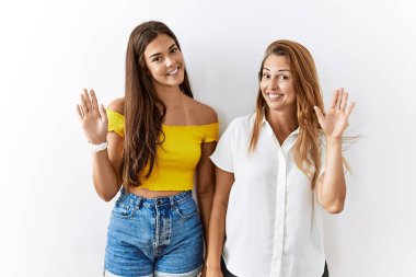 Anne ve kızı birlikte münzevi bir arka planda duruyorlar. Mutlu ve güler yüzlü bir şekilde selamlaşıyorlar. 