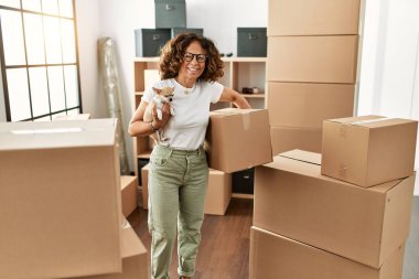 Orta yaşlı İspanyol kadın gülümsüyor. Yeni evinde kendine güvenen bir chihuahua tutuyor.