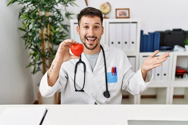 Young Doctor Holding Heart Medical Clinic Celebrating Achievement Happy Smile — Stockfoto