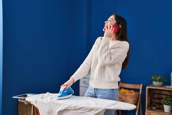 洗濯室でスマートフォンのアイロン掛け服について話す若い女性 — ストック写真