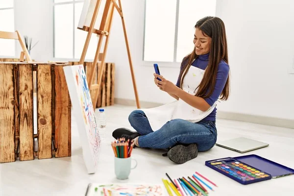 年轻的拉丁女子坐在艺术工作室的地板上画画 — 图库照片