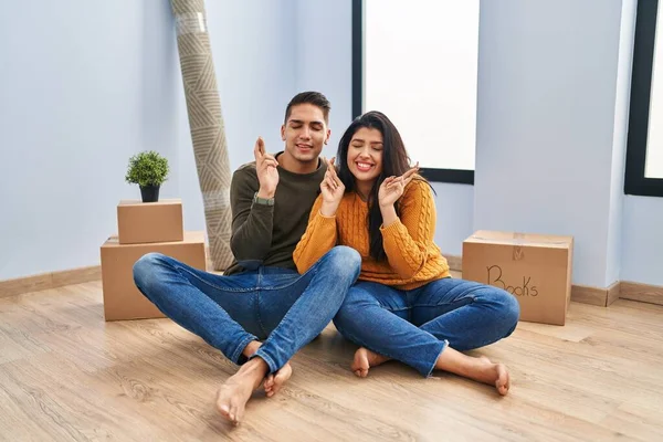 Young Couple Sitting Floor New Home Gesturing Finger Crossed Smiling — Stock Photo, Image