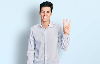 Genç İspanyol iş adamı iş kıyafetleri giyer ve üç numaralı parmaklarıyla gülümseyerek mutlu ve kendinden emin bir şekilde işaret eder.. 