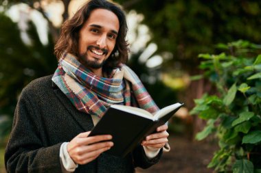 Genç İspanyol adam gülümsüyor. Parkta mutlu bir kitap okuyor..