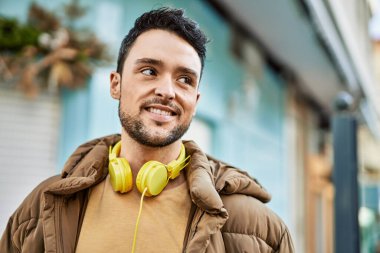 Şehirde kulaklık takarak mutlu gülümseyen genç İspanyol adam..