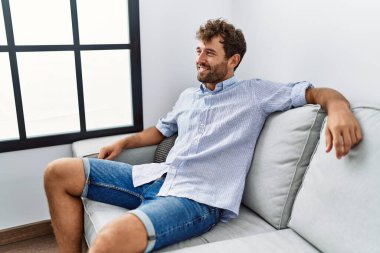 Evdeki kanepede mutlu gülümseyen İspanyol genç adam..