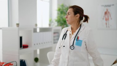 Orta yaşlı İspanyol kadın doktor üniforması giyiyor klinikte rahat bir ifadeyle dikiliyor.