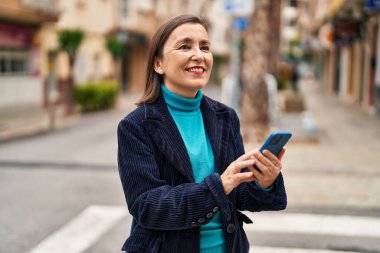 Sokakta akıllı telefon kullanan orta yaşlı bir iş kadını.
