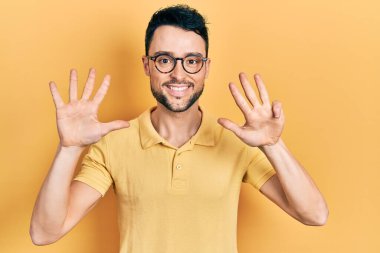 Gündelik kıyafetler giyen ve gözlük takan İspanyol genç adam dokuz numarayı gösterip işaret ederken kendinden emin ve mutlu bir şekilde gülümsüyor.. 