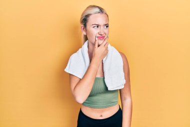 Spor kıyafetleri ve havlu giyen genç sarışın kız bir soru hakkında endişeli ve gergin bir şekilde düşünüyor. 