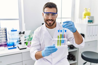 Laboratuvarda deney tüpü tutan bilim adamı üniforması giyen İspanyol genç adam.