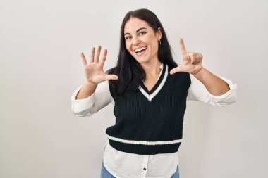 İzole edilmiş arka planda duran genç İspanyol kadın yedinci parmaklarını gösterip işaret ederken kendinden emin ve mutlu gülümsüyor.. 