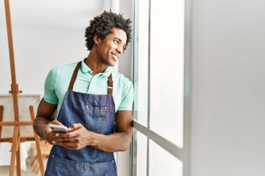Genç Afrikalı Amerikalı sanatçı, sanat stüdyosunda akıllı telefon kullanıyor..