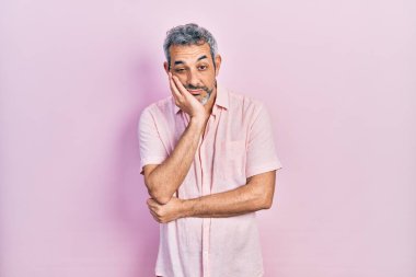 Yakışıklı, orta yaşlı, gri saçlı, rahat tişörtlü, yorgun ve bunalımda kollarını kavuşturmaktan sıkılmış görünen bir adam.. 