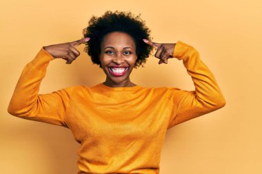 Genç Afro-Amerikan kadın, günlük giysiler giyip iki eliyle başını gösteren gülümseme, harika bir fikir ya da düşünce, iyi bir hafıza 