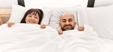 Yatak odasındaki yatakta çarşafla yüzünü örten genç İspanyol çift..