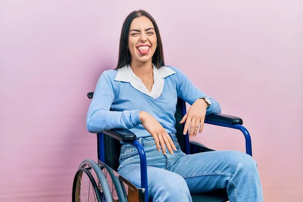 Beautiful woman with blue eyes sitting on wheelchair sticking tongue out happy with funny expression. emotion concept.