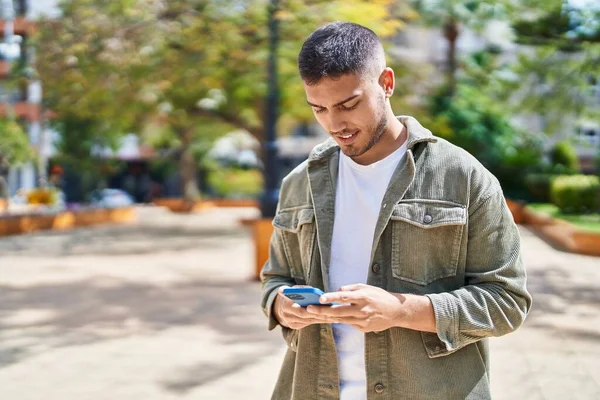 公園でスマートフォンを使って自信を持って笑っている若いヒスパニック系の男 — ストック写真