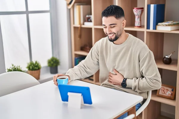 Young arab man watching movie and drinking coffee sitting on table at home