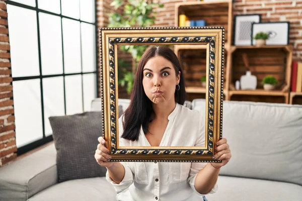 Young Hispanic Woman Holding Empty Frame Puffing Cheeks Funny Face — Stock Photo, Image