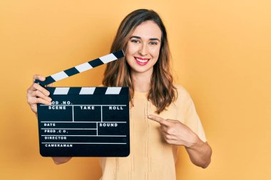 Young hispanic girl holding video film clapboard smiling happy pointing with hand and finger 