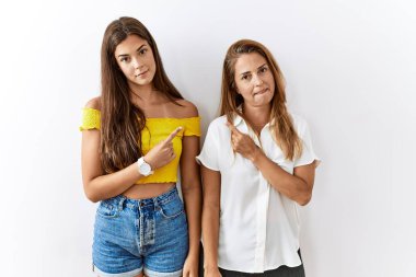 Anne ve kızı birlikte izole edilmiş arka planda yan yana duruyorlar. Elleriyle işaret ediyorlar. Ciddi ve sakin bir yüz ifadesi gösteriyorlar. 