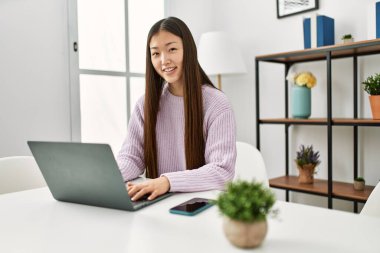 Young chinese girl using laptop sitting on the table at home.