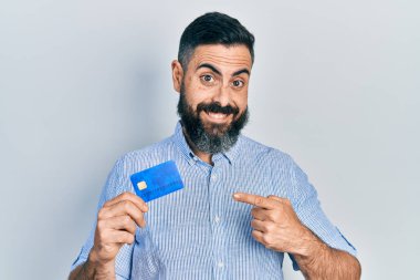 Kredi kartı tutan genç İspanyol adam mutlu bir şekilde el ve parmağıyla işaret ediyor. 