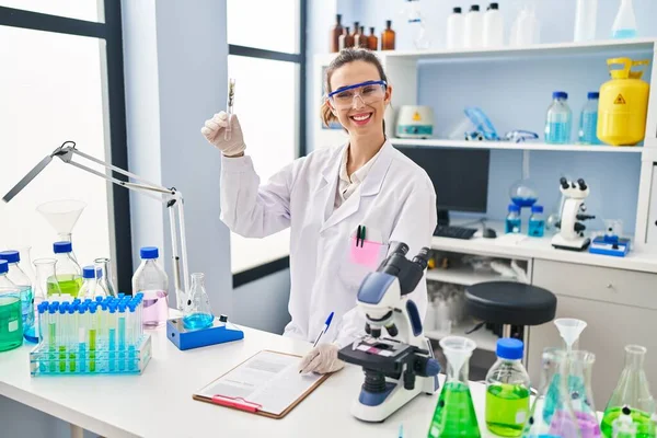 Young woman wearing scientist uniform analysing herb at laboratory