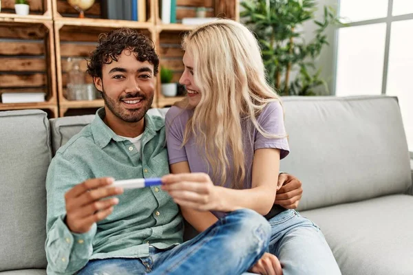 年轻夫妇在家里笑着高兴地看着怀孕的测试结果 — 图库照片