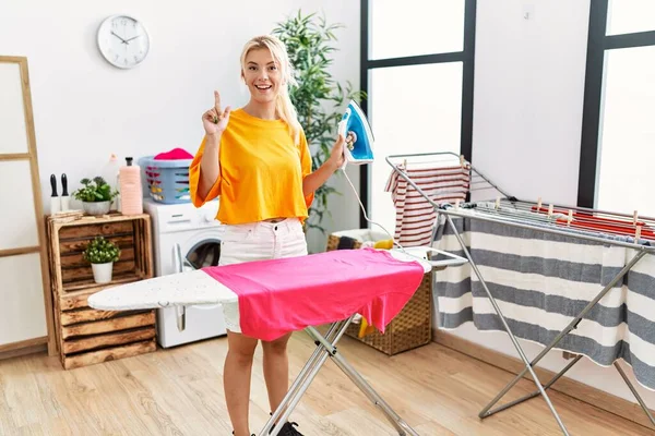 Young Caucasian Woman Ironing Clothes Home Surprised Idea Question Pointing — 스톡 사진