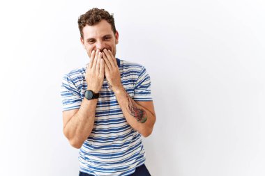 Yakışıklı genç adam izole edilmiş arka planda duruyor gülüyor ve utanıyor kıkırdıyor elleriyle ağzını kapatıyor, dedikodu ve skandal konsepti yapıyor. 