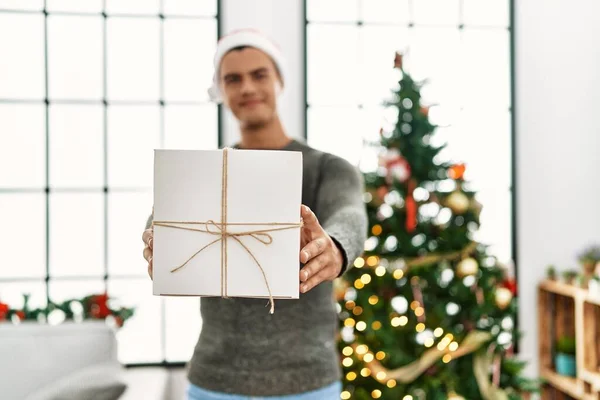 Young Hispanic Man Holding Gift Standing Christmas Tree Home — Stockfoto