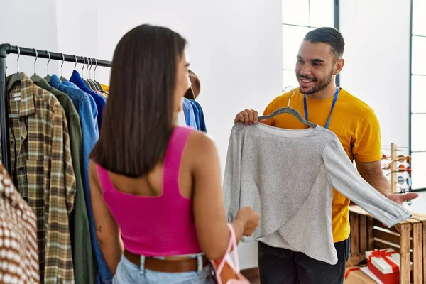 Young latin shopkeeper showing clothes to customer at clothing store.