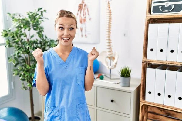 Young caucasian woman working at pain recovery clinic celebrating surprised and amazed for success with arms raised and open eyes. winner concept.
