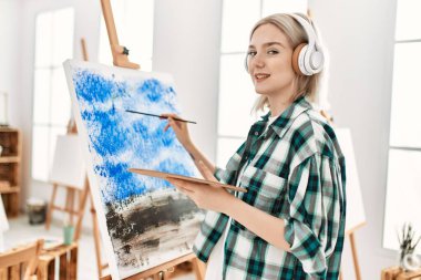 Sanat stüdyosunda resim yaparken ve müzik dinlerken gülümseyen genç sanatçı kız..